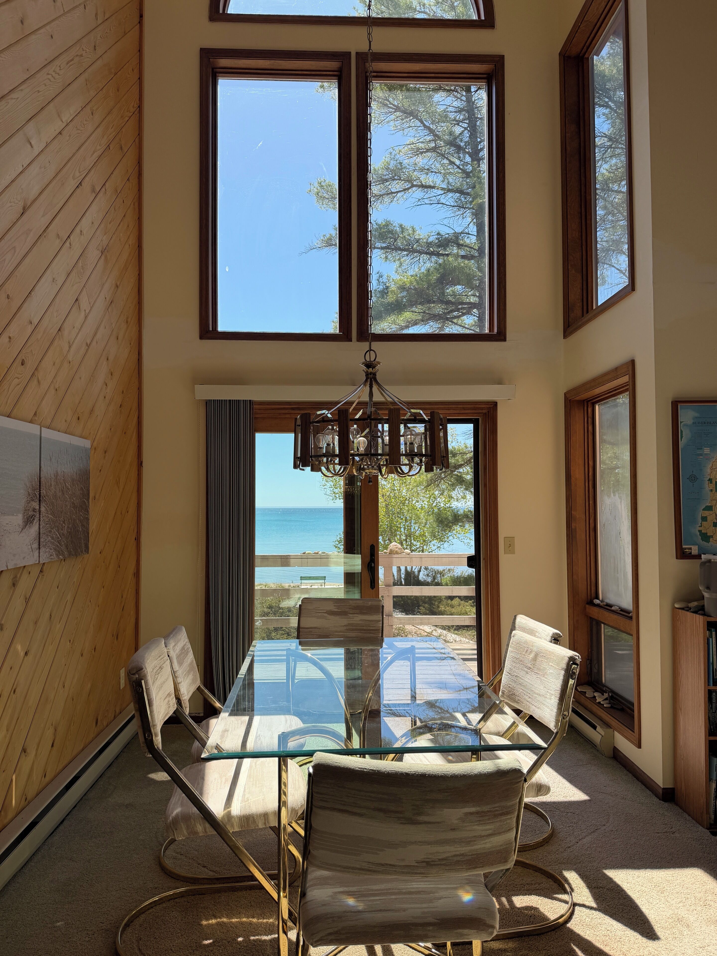 A dining area with a glass table and chairs, large windows, and a view of the sea.