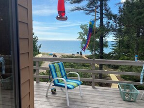 A wooden deck with a striped chair and a small ball, overlooking a beach with a flag and a red object.