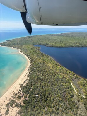 An aerial view of a coastal area with a beach, forest, and a body of water.