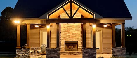 A poolside building with a stone fireplace, wooden beams, and a covered seating area.