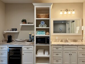 A bathroom with a built-in oven, a coffee maker, a microwave, and a vanity with a mirror.