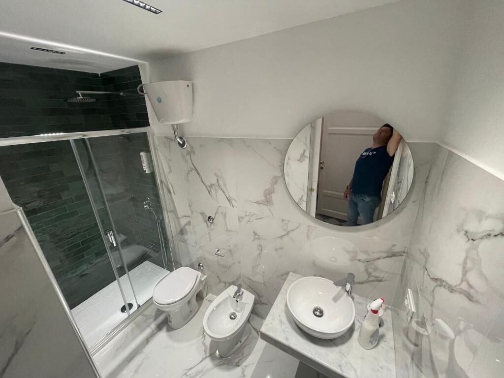 Un baño moderno con ducha de vidrio, dos inodoros, un bidé y un lavamanos de mármol.