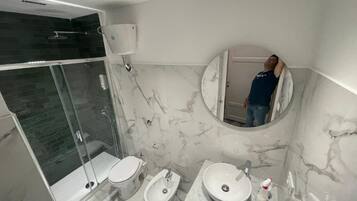 Un baño moderno con ducha de vidrio, dos inodoros, un bidé y un lavamanos de mármol.