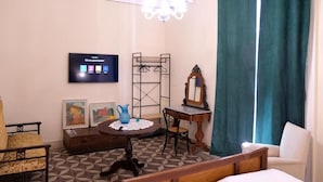 A room with a bed, a chair, a table with a vase, a TV mounted on the wall, and a window with curtains.
