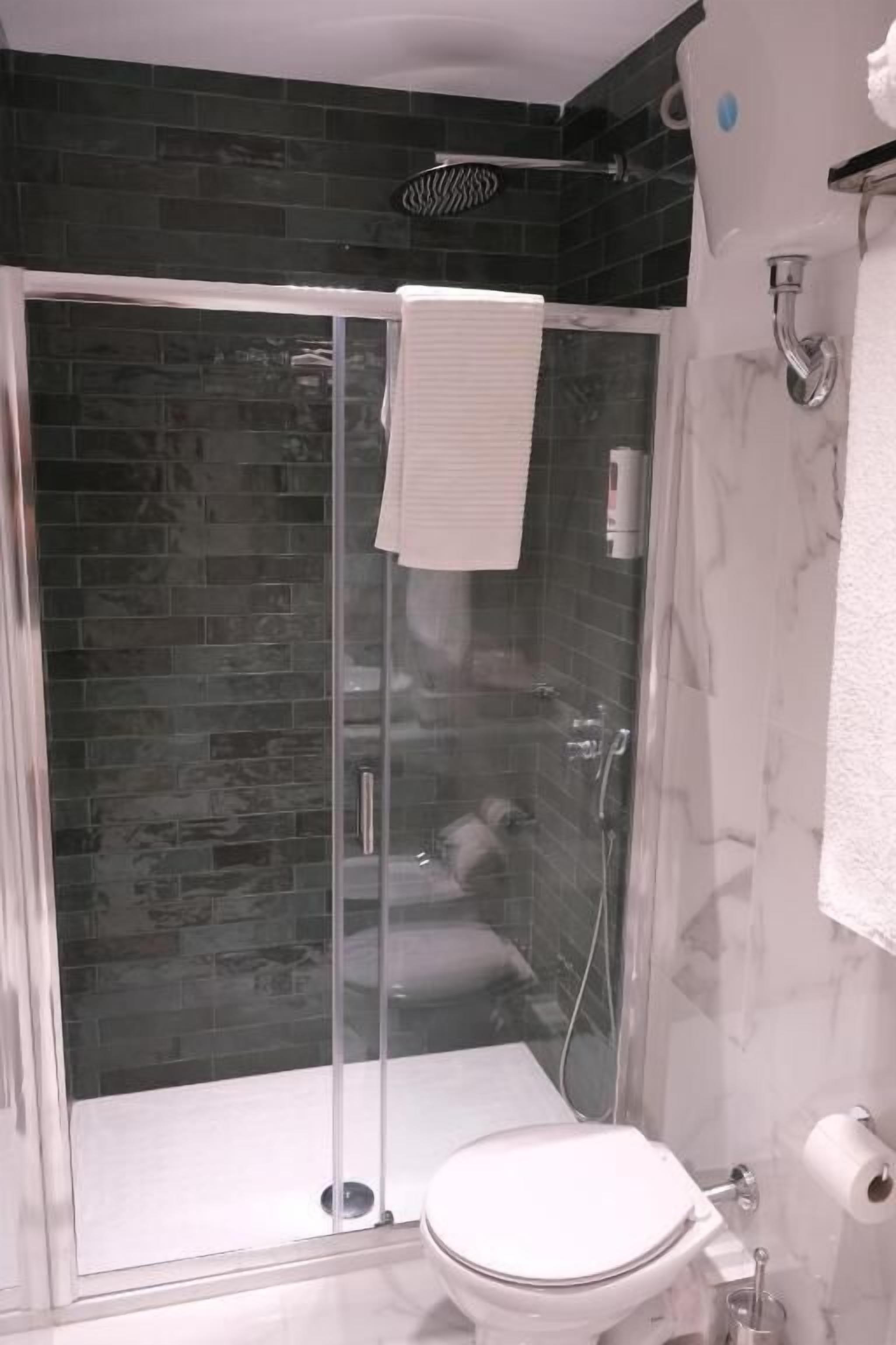 Un baño con ducha de vidrio, inodoro blanco y pared de mármol.