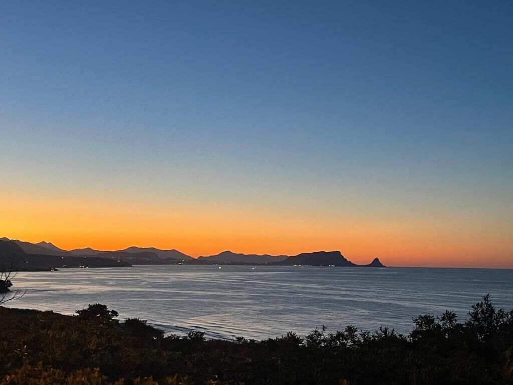 A coastal landscape with a clear sky, calm sea, and distant landforms.