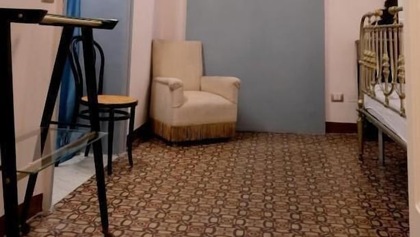 A room with a patterned floor, a large mirror, a chair, and a television.