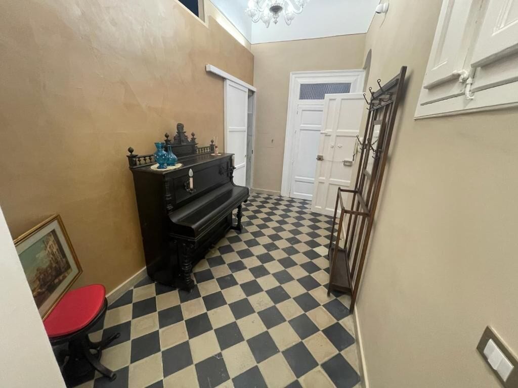 A hallway with a checkered floor, a piano, a red chair, and a door.