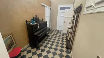 A hallway with a checkered floor, a piano, a red chair, and a door.