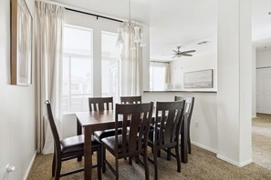 A dining area with a wooden table and chairs, a ceiling fan, and a view of the outside.