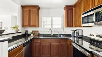 A kitchen with wooden cabinets, a black countertop, a stainless steel sink, a microwave, and a coffee maker.