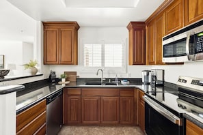 Cucina con mobili in legno, un piano di lavoro nero, un lavello in acciaio inossidabile, un forno a microonde e una macchina per il caffè.