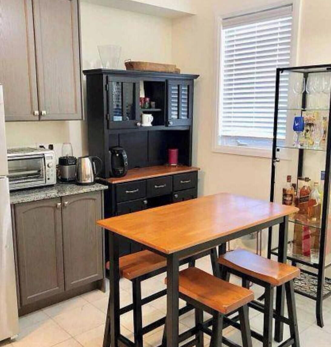 A kitchen with a wooden table and bar stools, a black cabinet with kitchen appliances, and a refrigerator with items on the door.