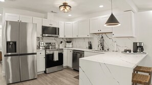 A modern kitchen with white cabinetry, stainless steel appliances, a marble backsplash, and a central island. - Tampa Family Home with Putting Green + Fenced Yard (Tampa)