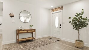 Een hal met een houten console tafel, een ronde spiegel, een potplant en een deur met een decoratief bord.