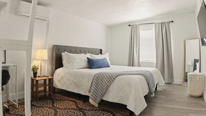 Een slaapkamer met een bed, nachtkastje, lamp en een raam met gordijnen.