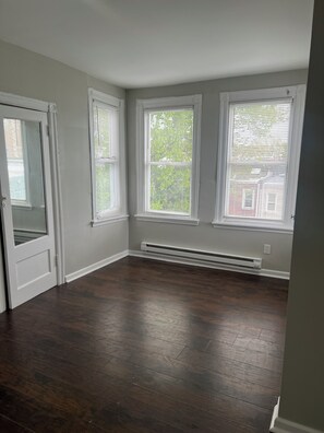 A room with three windows, a door, and a built-in heater. - Cozy 1-bedroom apartment in lovely Philadelphia with AC (Philadelphia)