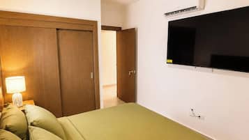 A room with a bed, a nightstand with a lamp, a wooden wardrobe, and a wall-mounted TV.