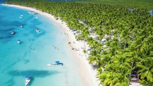 A beach with clear turquoise waters, boats, and a line of palm trees. - ANYA 6 Downtown Bayahíbe Retreat Pool  (Bayahíbe)