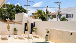 A swimming pool with lounge chairs and umbrellas, surrounded by a white wall and palm trees. - ANYA 6 Downtown Bayahíbe Retreat Pool  (Bayahíbe)