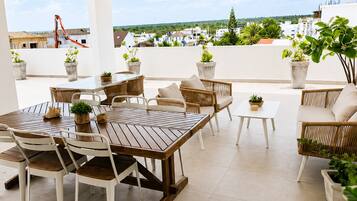 Kattoterassi, jossa on puinen pöytä ja tuolit, ruukkukasveja ja näkymä kaupunkimaisemaan.