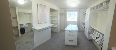A walk-in closet with mirrored doors, a vanity with a mirror, and multiple storage shelves.