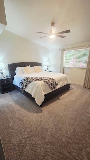 A bedroom with a bed, nightstands, a ceiling fan, and a window with blinds.