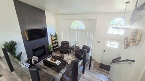 Una sala de estar con chimenea, sofás de cuero, una mesa de centro de vidrio y un televisor montado en la pared.