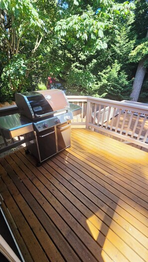 A barbecue grill on a wooden deck with a railing, surrounded by trees.