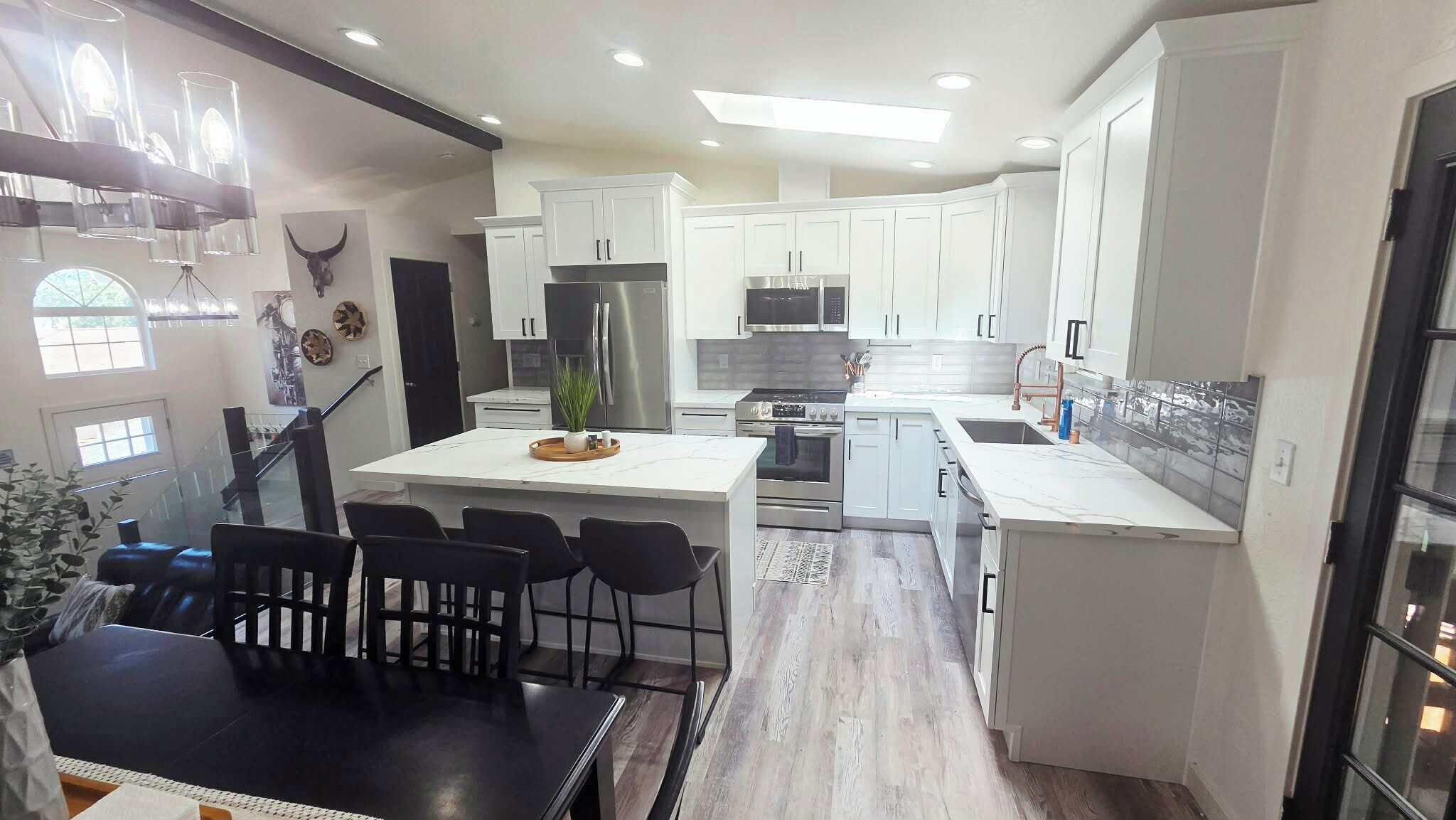 A modern kitchen with white cabinetry, stainless steel appliances, and a central island with bar stools.