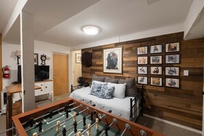 A cozy room with a bed, a foosball table, and a wall decorated with framed pictures. - Delightful cabin Sleeps 14! 5 Min To Pinecrest Lake! Family Gatherings Welcome! (Long Barn)