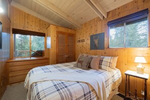 Une chambre dans une cabane en bois, avec un lit, une table de chevet, une fenêtre et une porte.