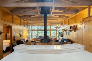 Une pièce spacieuse avec une grande table centrale, des murs en bois et un plafond haut avec des poutres apparentes.