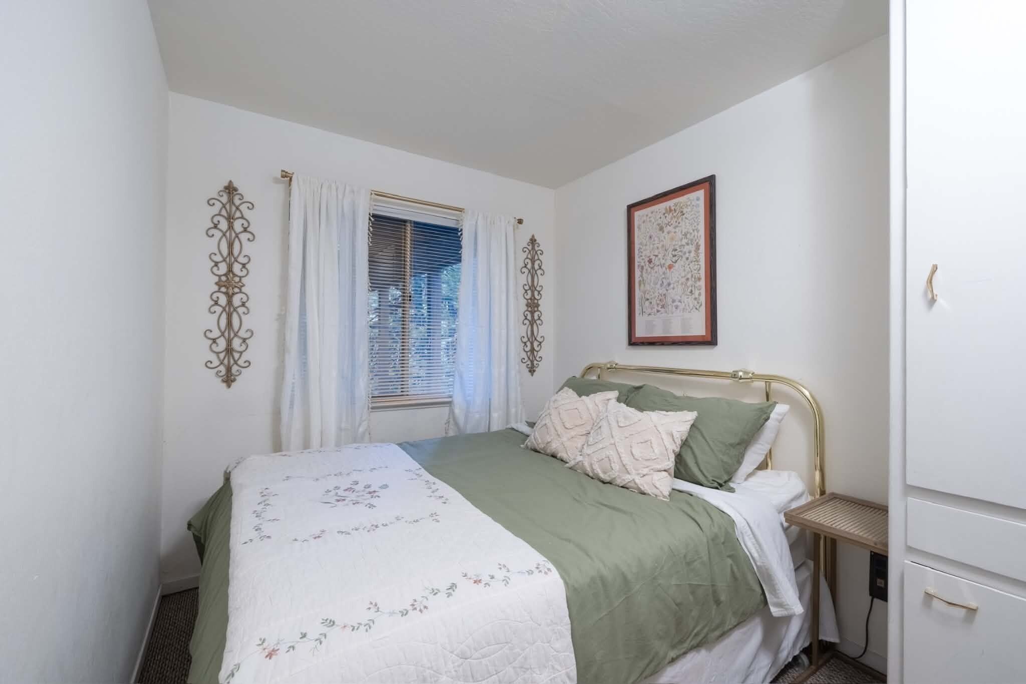 Une chambre à coucher avec un lit, des rideaux, un tableau encadré et une table de chevet.