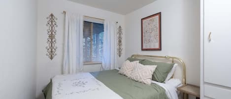 A bedroom with a bed, curtains, a framed picture, and a bedside table.