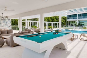 A pool area with a pool table, lounge chairs, and a view of a modern building. - Chic Poolside Condo with Ocean Views (West Bay)