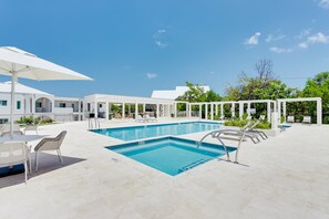 Una piscina amb gandules i ombrel·les, envoltada d'un edifici blanc amb moltes finestres.