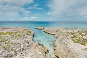 A rocky coastal landscape with clear turquoise waters and sparse vegetation. - Chic Poolside Condo with Ocean Views (West Bay)