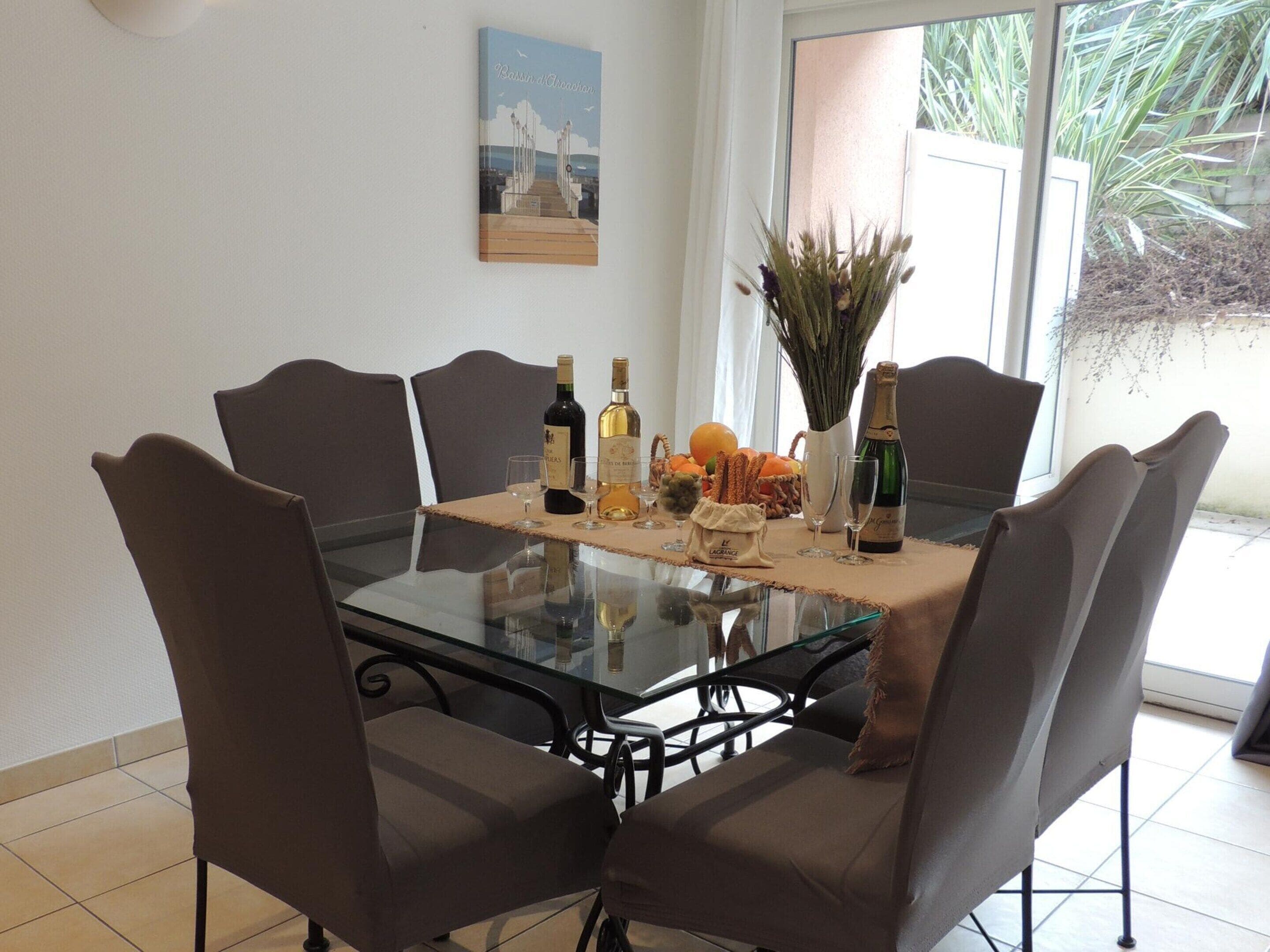 A dining table with six chairs, a glass top, and a variety of food and drink items.