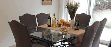 Una mesa de comedor con seis sillas, superficie de vidrio y diversos alimentos y bebidas.