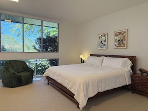 A bedroom with a large window, a bed, a green chair, and two wall-mounted artworks.