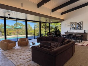 A spacious living area with a large sectional sofa, a coffee table, and a view of a swimming pool and outdoor seating.
