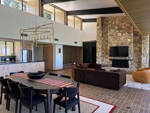 A modern interior with a dining area, kitchen, stone fireplace, and a flat-screen TV mounted on a stone wall.
