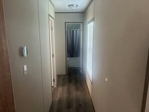 A narrow hallway with a wooden floor, a door on the left, and a window with blinds on the right.