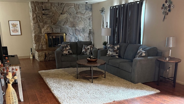 A living room with a stone wall, a gray sofa, a coffee table, and a lamp. - Spacious 5-bedroom house in Sturgis South Dakota! (Sturgis)