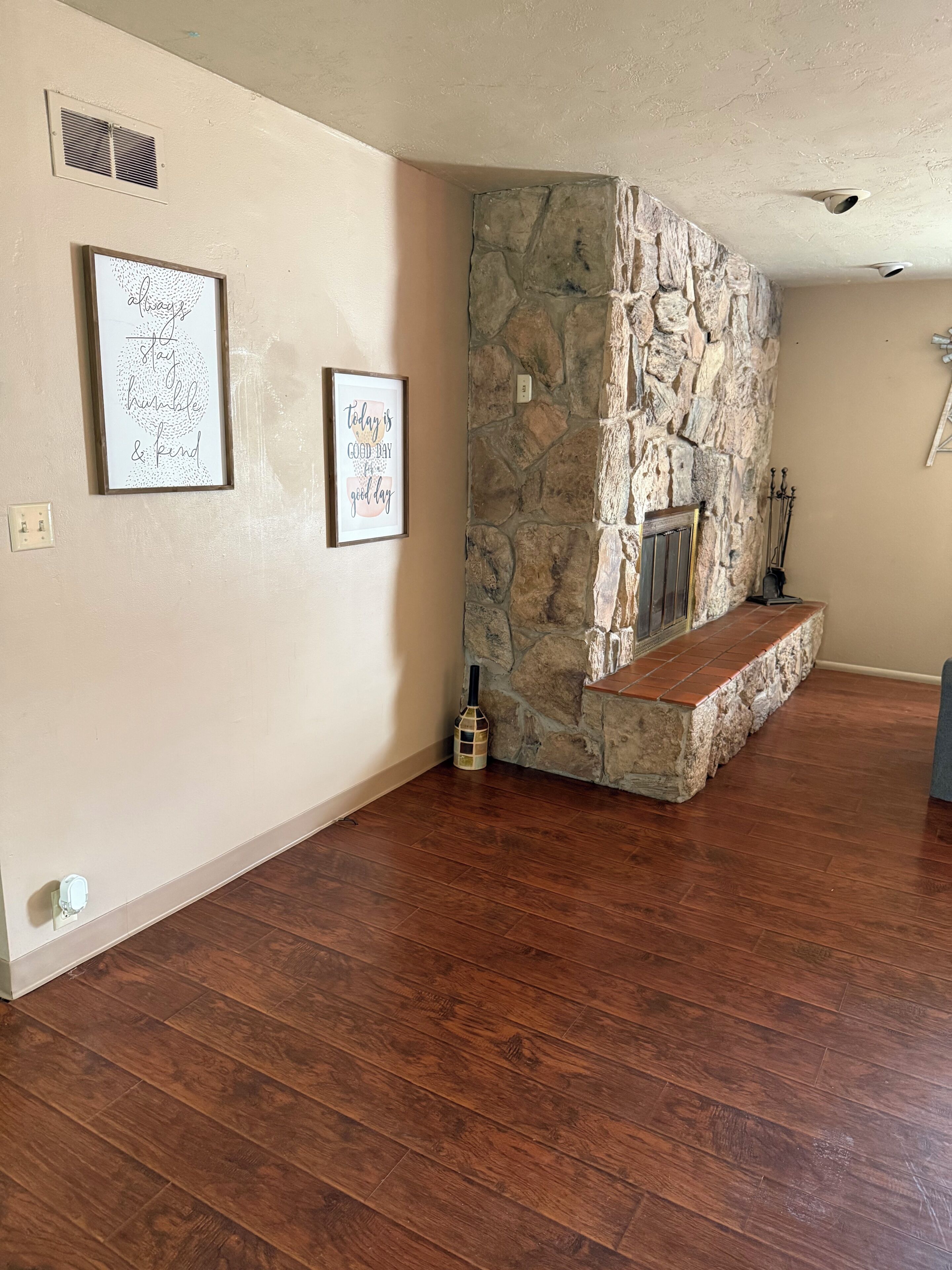 A room with a stone fireplace, wooden flooring, and two framed motivational quotes on the wall.
