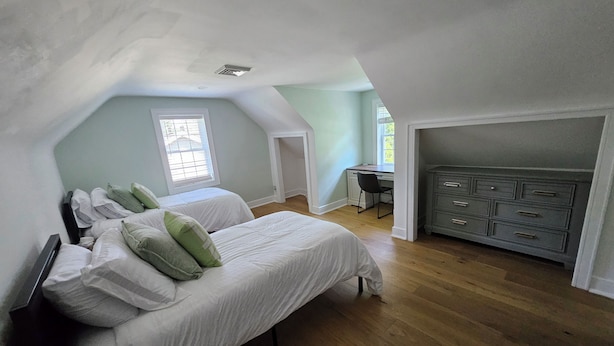 A bedroom with a lofted desk area, a bed with pillows, and a dresser.