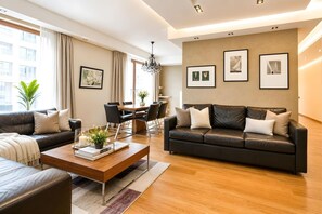 Een moderne woonkamer met een leren bank, een houten salontafel en een eethoek met tafel en stoelen.