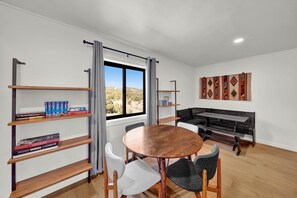 A modern living room with a round wooden table, two chairs, a bookshelf, a sofa, and a window with a view of a desert landscape. - The King Ranch I South Fork, Colorado Retreat (South Fork)