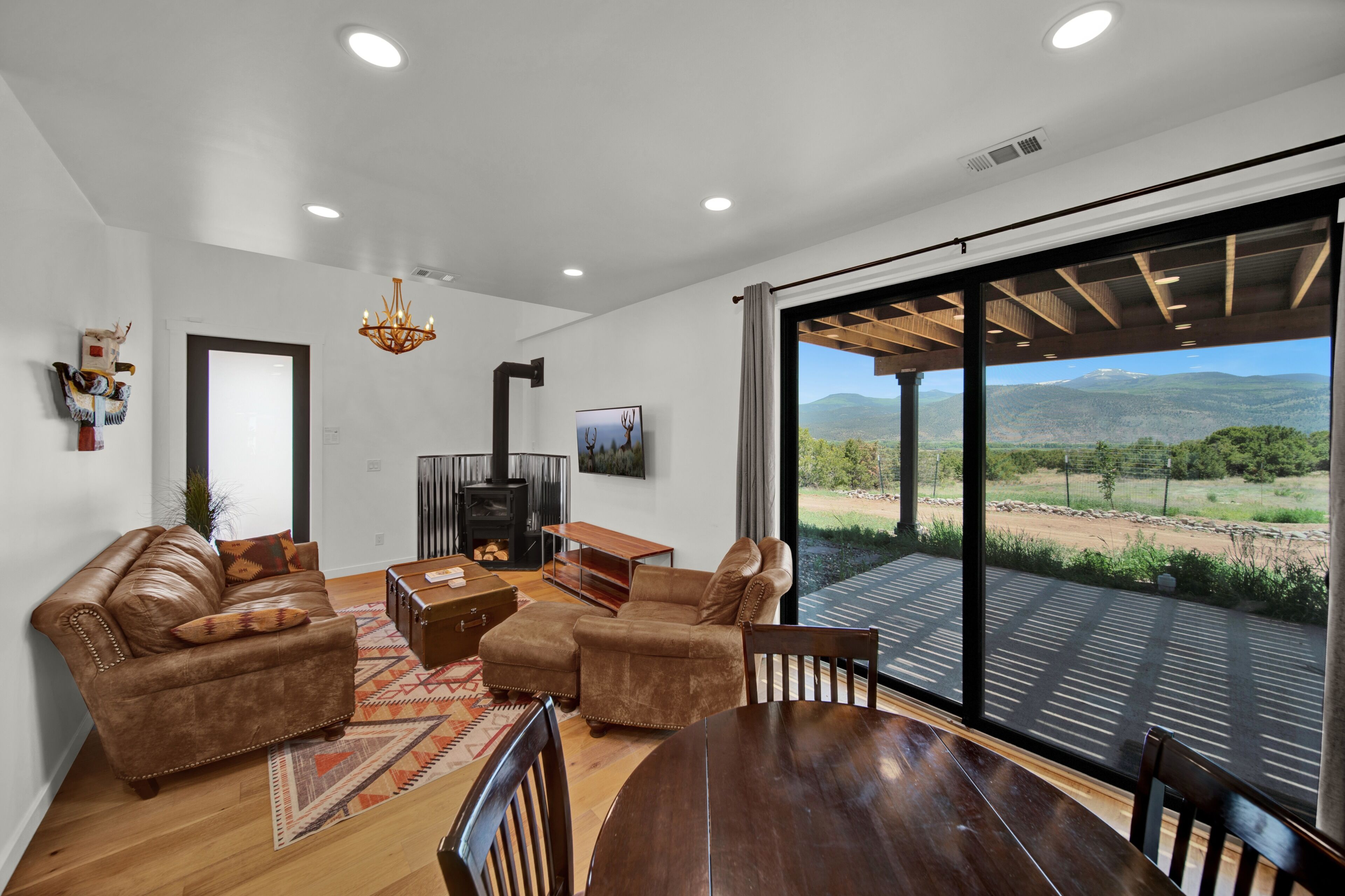 A modern living room with a fireplace, leather sofas, a wooden coffee table, and a large sliding glass door leading to a patio with a mountain view.